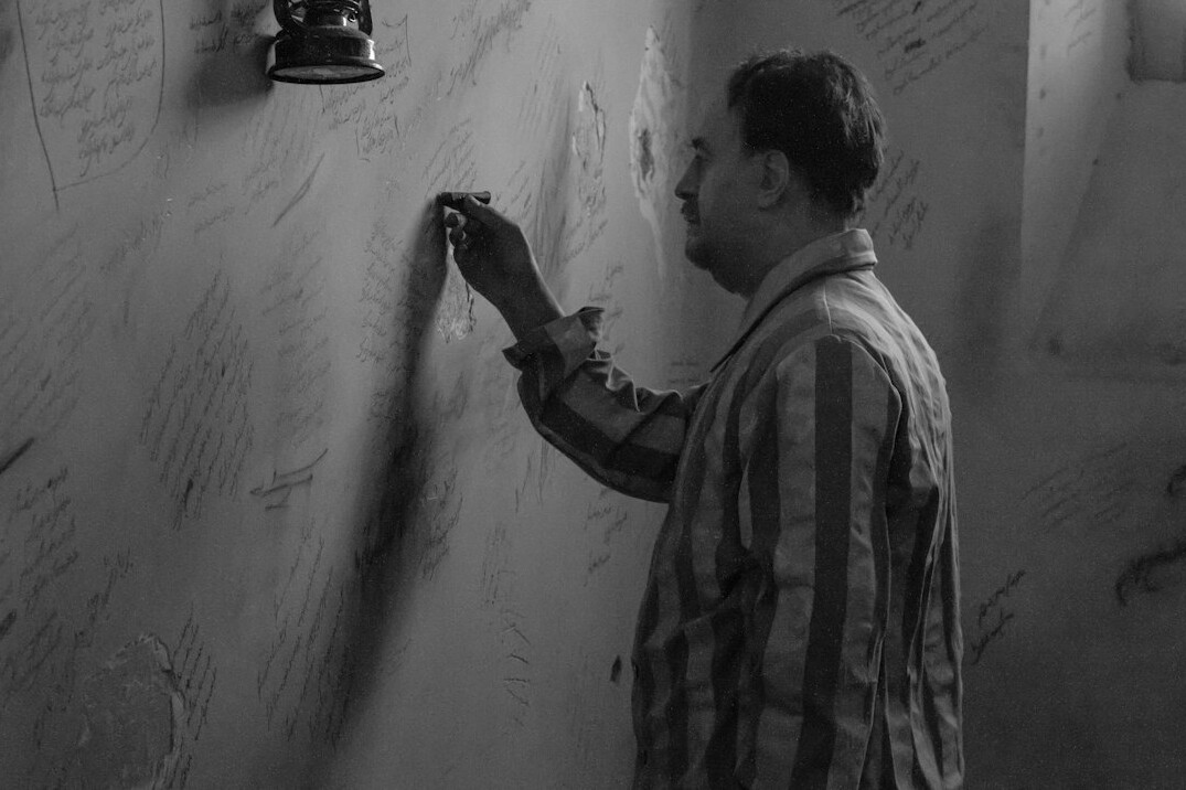 Man in a trench coat examining a letter with a flashlight
